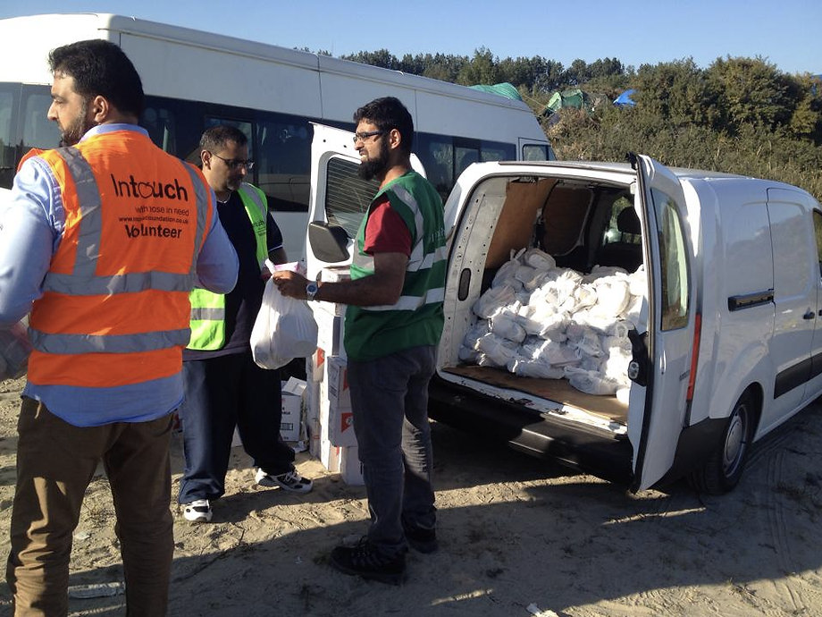 Three men in high-vis jackets standing in front of a van filled with lots of white plastic bags.